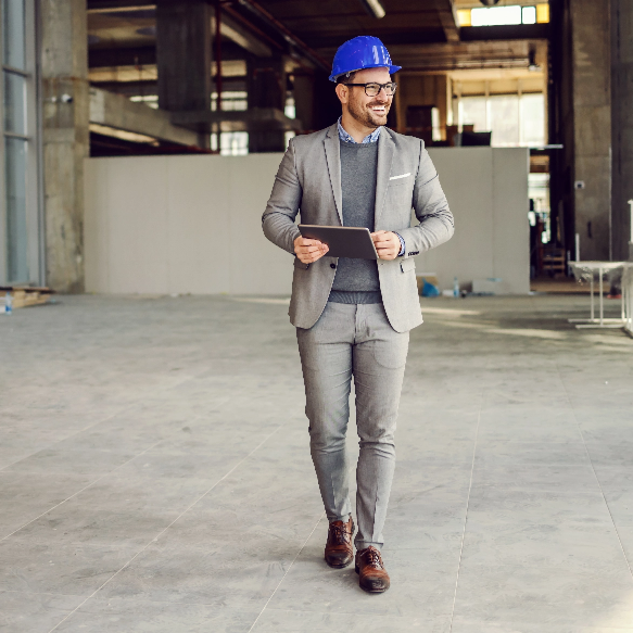 Building for Success: Nautilus Commercial Property Insurance Safeguards Your Investments A man wearing a suit and hardhat smiles while holding a tablet and walking through a high-rise building that is under construction.